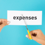 Person cutting a piece of paper with the word expenses on it for small business finances