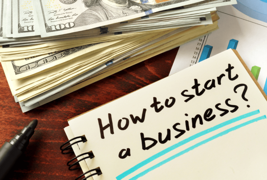 money, charts, and notebook with how to start a business written on it